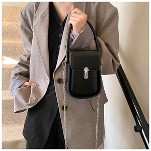 Mini black leather shoulder bag with silver clasp and chain strap on a grey suit model