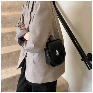 Detail of a black glossy leather mini bag with silver chain strap worn by a model