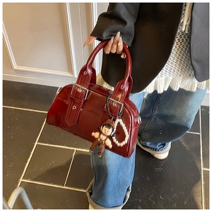 Detail view of burgundy Boston bag with glossy finish, doll charm and pearl chain decoration