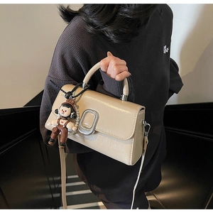 Detail view of beige matte leather handbag with silver metal buckle and cute doll charm
