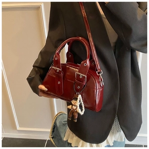 Detail of burgundy glossy Boston bag with pearl chain and doll charm accessory