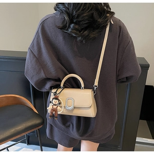 Detail of beige luxury crossbody bag featuring a silver buckle and boy doll charm