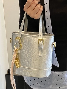 Silver metallic bucket bag with gold hardware and pink silk scarf detail shown in hand