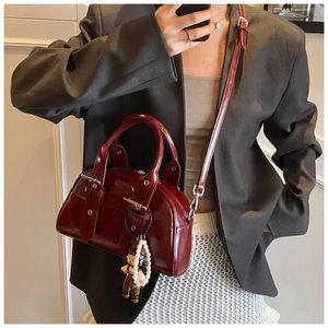 Detail of burgundy Boston bag with glossy leather texture and cute pearl doll charm