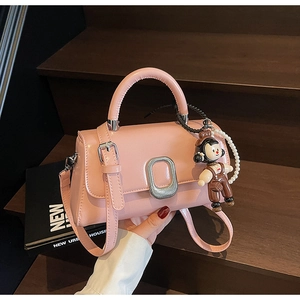 Close-up of pink luxury handbag with silver buckle, pearl chain and cartoon pendant