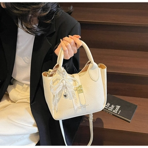 Detail view of cream lychee texture bucket bag with gold lock and pearl lace bow charm