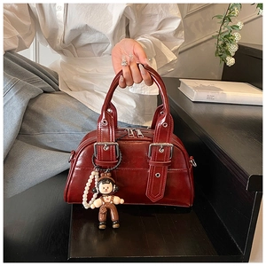 Detail of dark red glossy leather Boston bag with metal buckle and pearl charm accessory