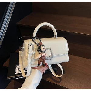 Detail of off-white square handbag with silver buckle and pearl doll charm on wooden steps