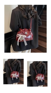 Détail du sac coquille bordeaux avec nœud en dentelle blanche et pendentif cœur