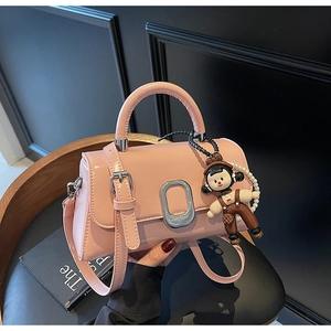 Detail of pink faux leather handbag featuring silver oval buckle and pearl doll charm
