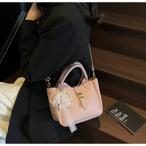 Close-up of pink litchi grain leather bucket bag with lace bow and gold lock hardware