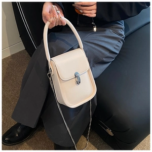 Detail shot of a cream leather handbag with silver chain strap and metal swivel lock on a sofa
