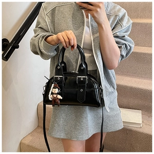 Detail of black glossy Boston bag with silver studs, doll charm, and pearl chain strap