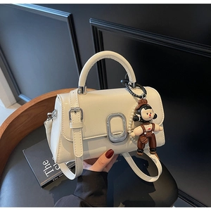 Detail of cream square leather bag featuring silver oval buckle and cute doll charm