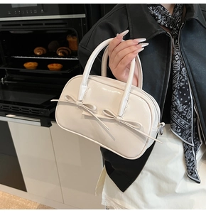 Détail du sac Boston blanc crème avec doubles nœuds décoratifs et texture brillante