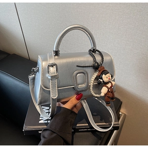 Detail of silver metallic handbag with oval buckle and cute doll charm on leather seat