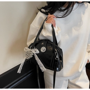Détail du sac coquille en cuir verni noir avec fermoir argenté et nœud en dentelle