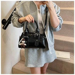 Close-up of black patent leather Boston bag featuring silver studs and a cute doll pendant