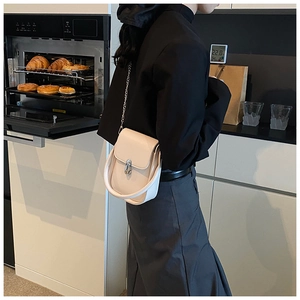 Detail shot of cream white crossbody bag with silver buckle and chain in a modern setting
