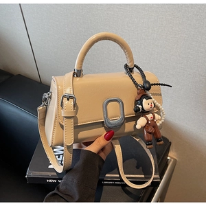 Detail view of beige crossbody bag with silver buckle and pearl charm accessory