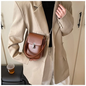 Detailed view of brown leather crossbody bag with silver clasp and metal chain strap