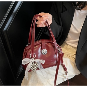 Détail d'un sac en cuir brillant bordeaux avec garniture argentée et nœud en dentelle