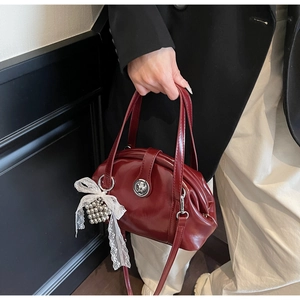 Détail d'un sac à main bordeaux brillant avec boucle argentée et charm nœud dentelle