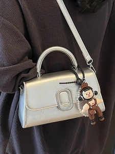 Silver metallic square handbag with metal buckle and detachable charm on a grey background