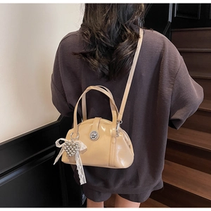 Sac à bandoulière beige avec pendentif coeur et nœud porté par un mannequin