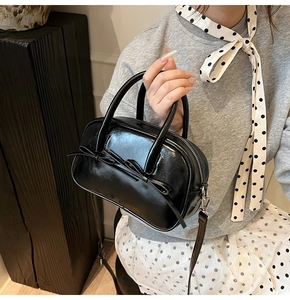 Détail du sac Boston en cuir noir avec un nœud élégant et des poignées supérieures