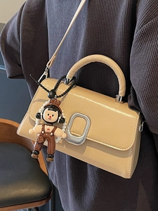 Elegant beige flap top handle bag with silver oval buckle and a beaded doll charm