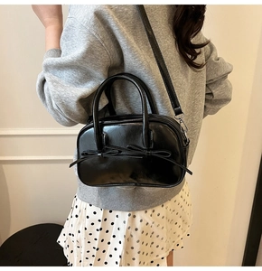 Sac Boston noir verni avec détails de nœuds porté en bandoulière sur un mannequin