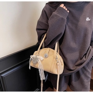 Détail du sac beige avec finition brillante, breloques en cœur et détails en ruban dentelle