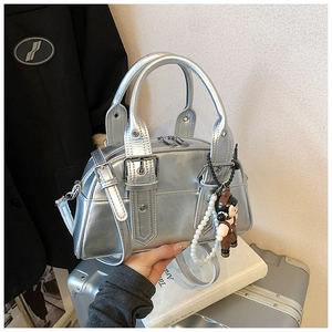 Detail of silver metallic Boston bag with buckle straps and a cute pearl doll charm