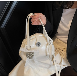 Détail du sac coquille blanc avec breloque cœur et nœud en dentelle à la main
