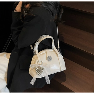 Sac docteur blanc avec charm cœur perlé porté sur un blazer noir sur des marches