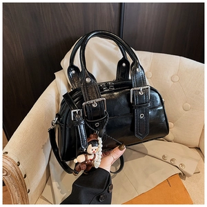 Detail of black patent leather Boston bag with metal buckles and decorative charm