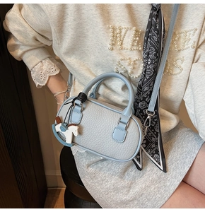 Dettaglio borsa a bauletto azzurra con trama litchi, ciondolo cavallo e foulard di seta