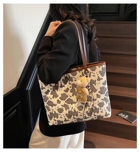 Detail view of cow print tote bag with brown leather strap and a cute teddy bear charm