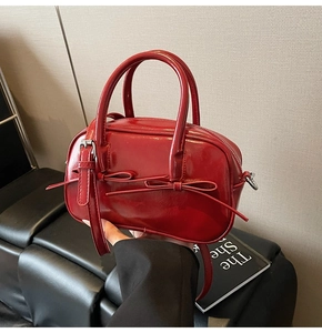 Détail du sac Boston en cuir verni rouge avec un nœud mince et des ferrures argentées
