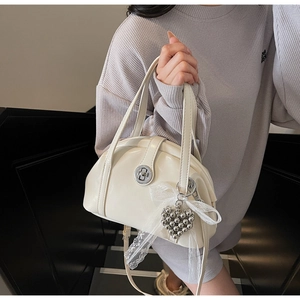 Détail du sac beige avec fermoir rond argenté et pendentif coeur en dentelle décorative