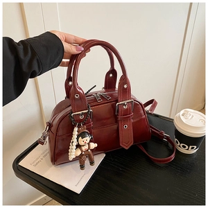 Detail of burgundy Boston bag with glossy texture, dual handles and a long shoulder strap