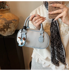 Dettaglio borsa a bauletto in pelle azzurra con ciondolo a cavallo e foulard di seta decorativo