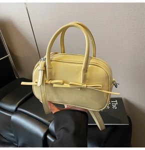 Détail du sac à main en cuir verni jaune crème avec nœud décoratif et poignées hautes