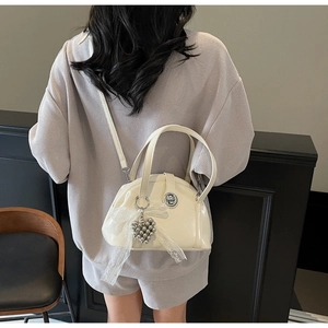Sac coquille crème chic avec nœud en dentelle et breloque cœur perlé sur un mannequin