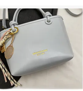 Detail of light blue crossbody bag featuring a golden tennis racket charm and woven strap