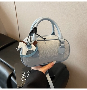 Dettaglio mini borsa boston azzurra con motivo litchi, ciondolo a cavallo e piedini