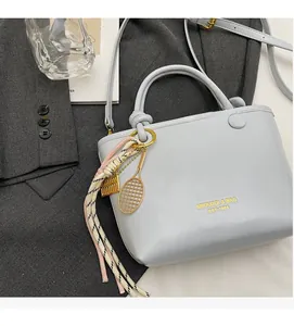 Detail of light blue leather bucket bag with gold lettering and decorative tennis charm