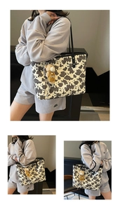 Detail of large cow print tote bag with long black straps and a cute teddy bear pendant
