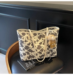 Detail of cow print tote bag featuring a cute plush bear charm on a leather seat
